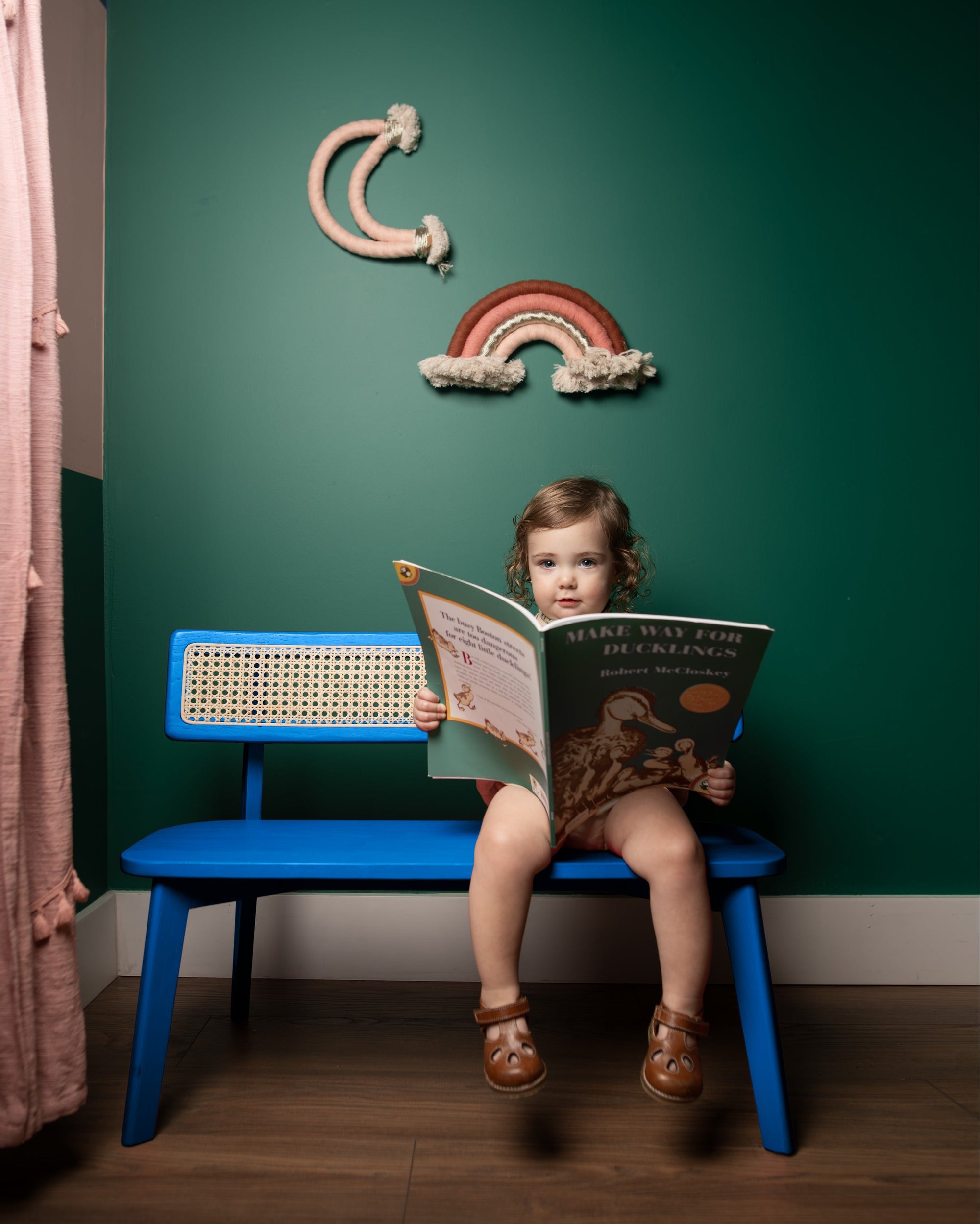 Child reading a book on a blue chair against a green wall with decorative moon and rainbow.